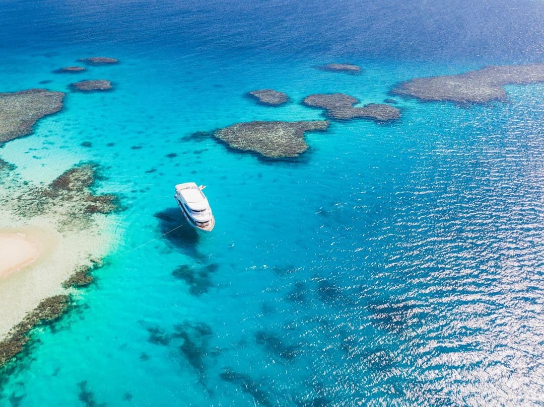 Aerial view of a boat anchored over turquoise reefs and sandbanks in the Red Sea near Marsa Alam